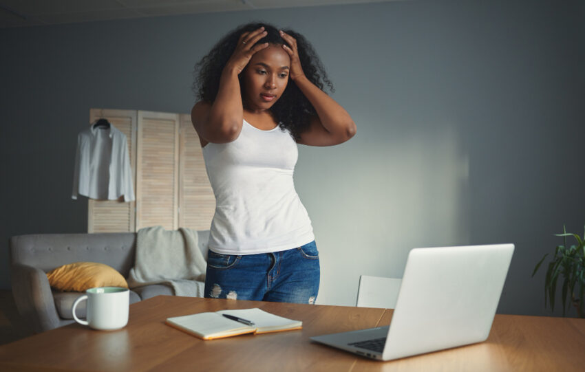 Jovem negra com as mãos na cabeça em frente a um computador